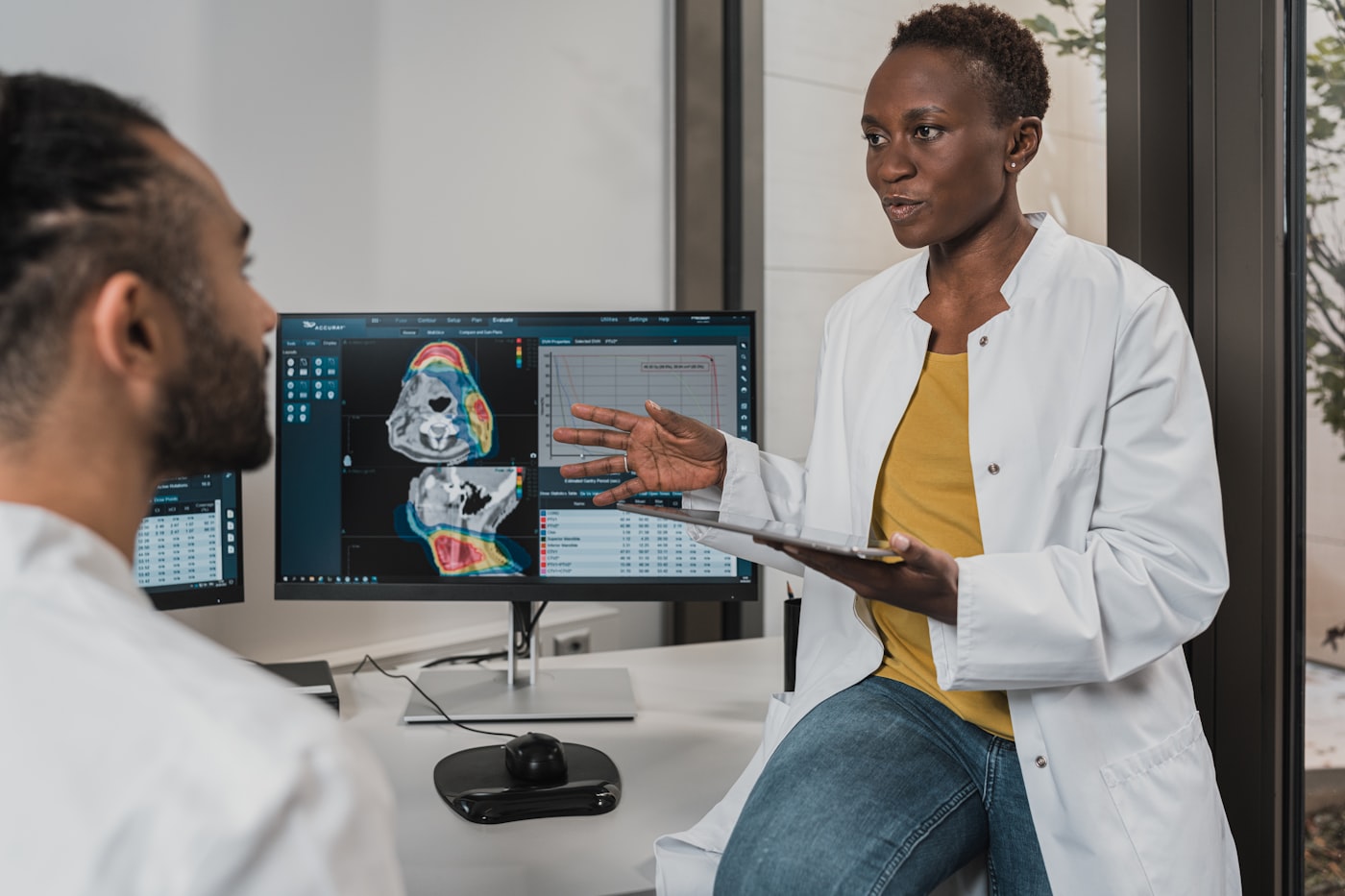 Two clinicians in white coats discussing diagnostic imaging displayed on a monitor.